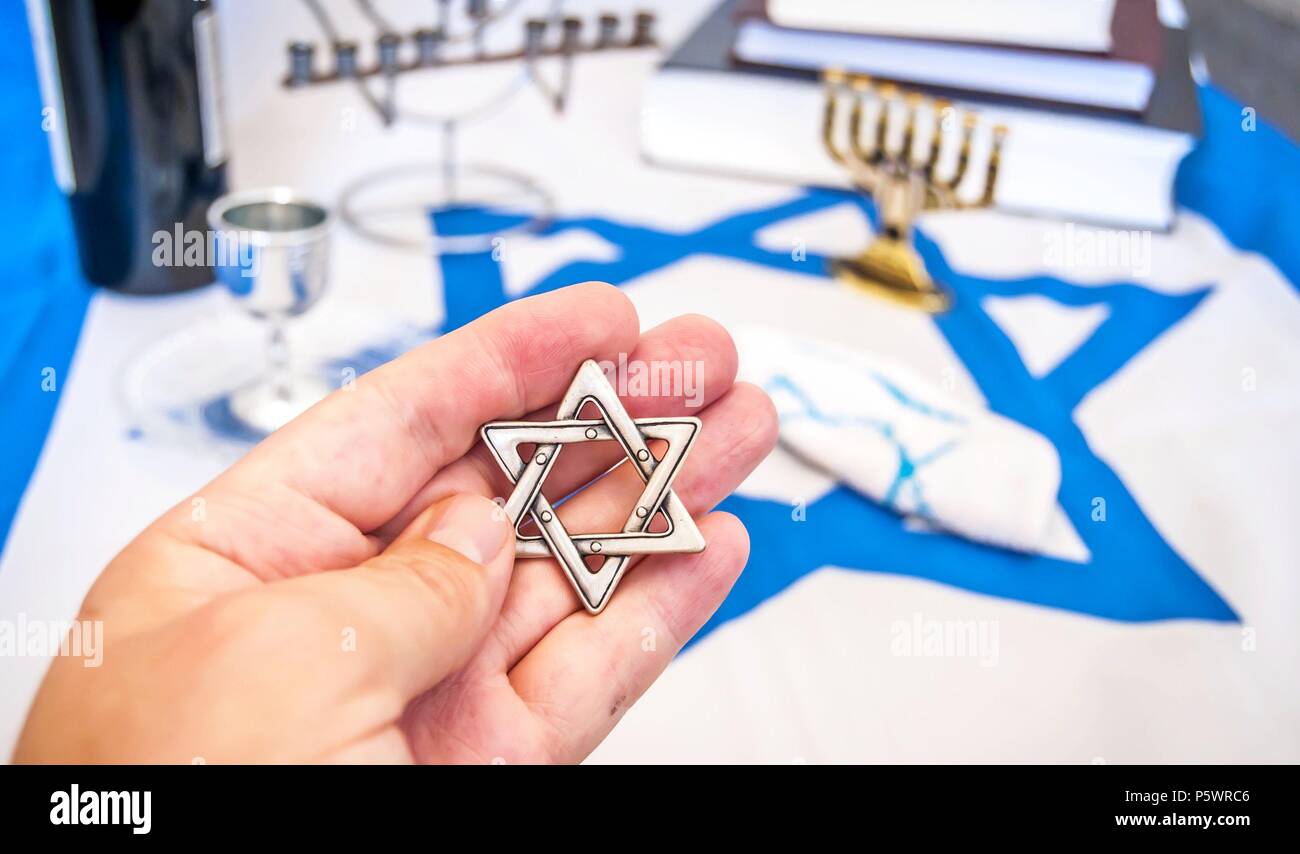 Mano che tiene una stella di Davide ('Magen David' in ebraico), un tradizionale ebraica simbolo religioso. Più simboli ebraici sullo sfondo: Libro di preghiera, menora Foto Stock