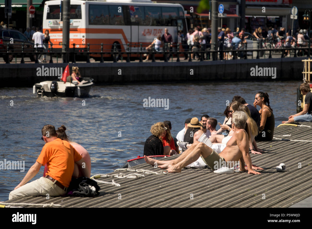 AMSTERDAM, PAESI BASSI - Maggio 10, 2018: turisti prendere un bagno di sole sulle rive di un canale di Amsterdam durante una giornata di primavera Foto Stock