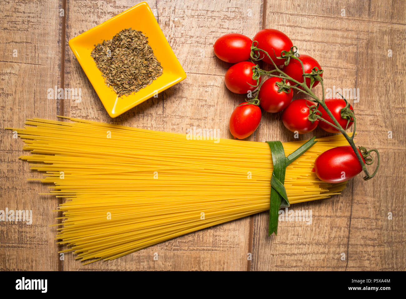 Gli spaghetti e Roma i pomodori isolate su tavola di legno dello sfondo. Non cotti italiano spaghetti secchi. Vista dall'alto. Lay piatto. Foto Stock