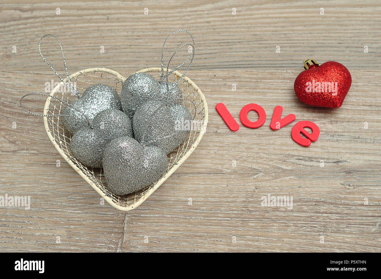 Un cestello in filo metallico riempito d'argento con forma di cuore baubles e la parola amore e una pallina rossa Foto Stock