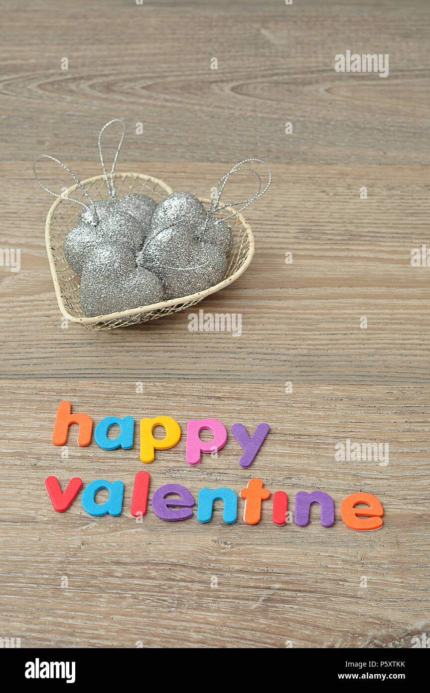 Un cestello in filo metallico riempito d'argento con forma di cuore baubles e le parole happy valentine Foto Stock