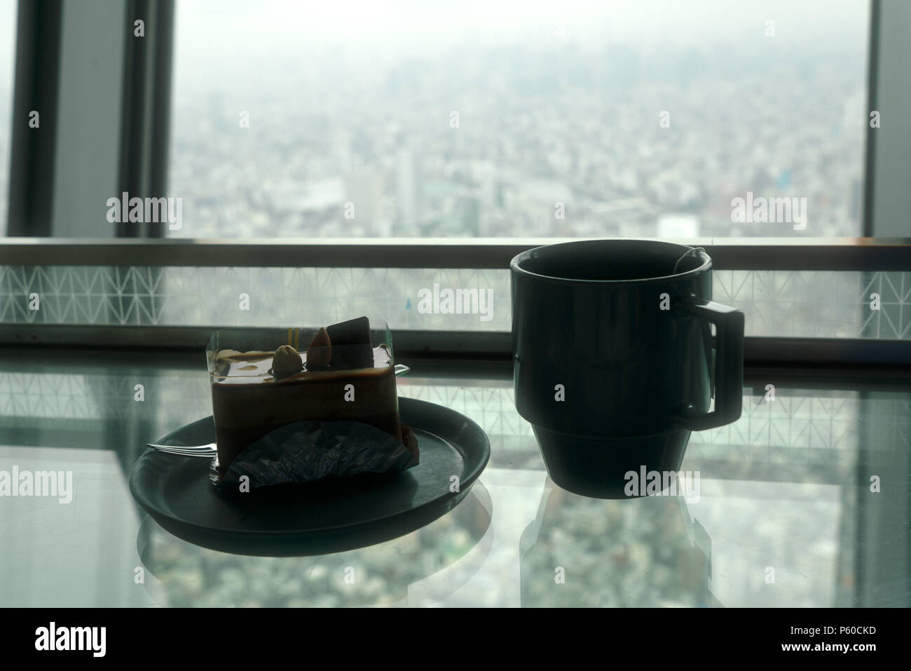 Tazza di tè e una fetta di torta sul tavolo di vetro contro vista città Foto Stock