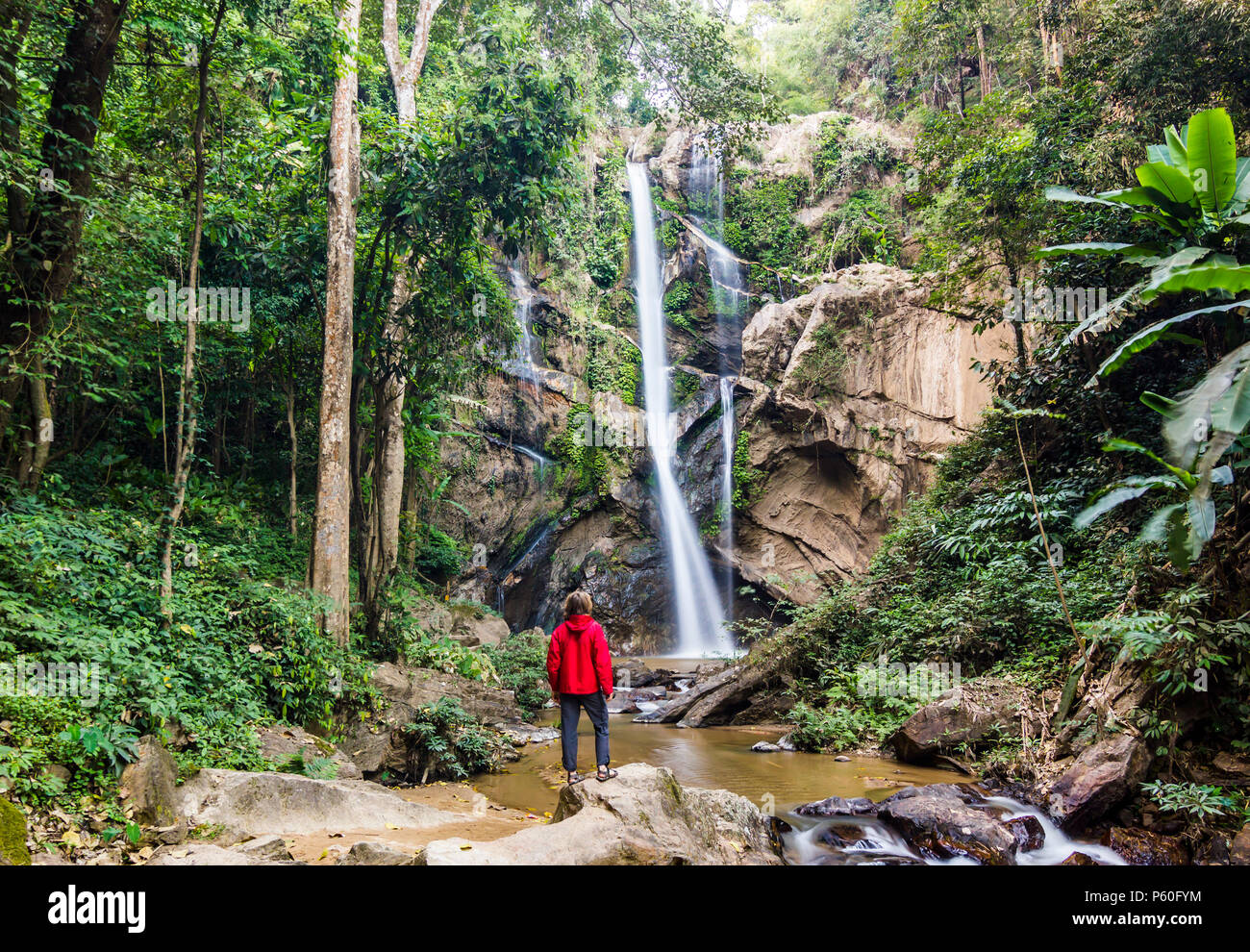 Uomo in piedi nella foresta vicino enorme cascata nella giungla della Thailandia Foto Stock
