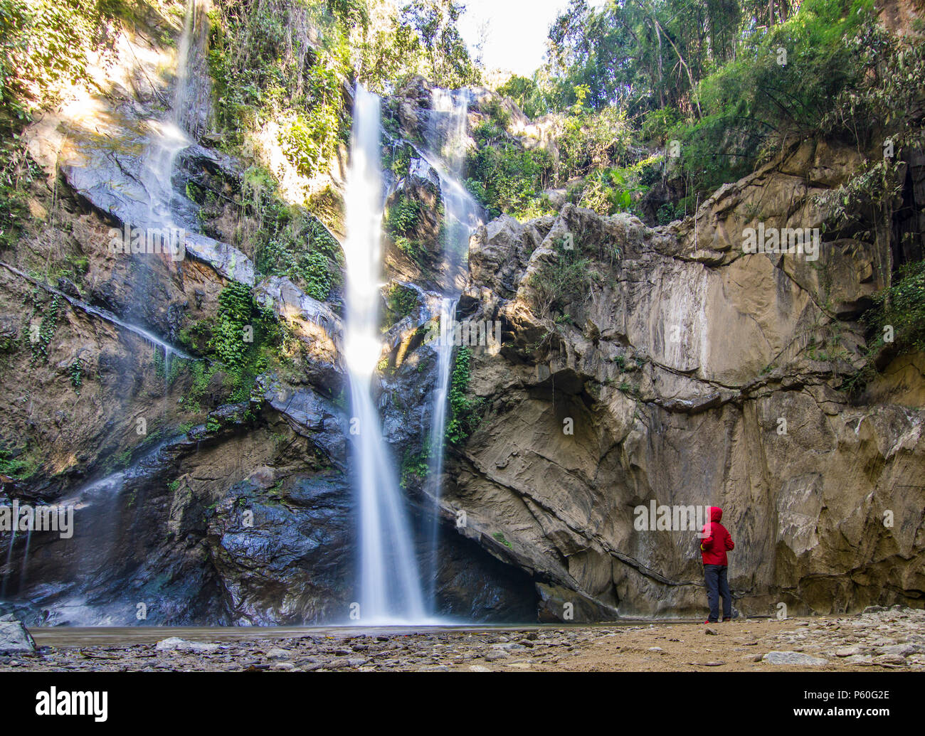 Uomo in piedi nella foresta vicino enorme cascata nella giungla della Thailandia Foto Stock