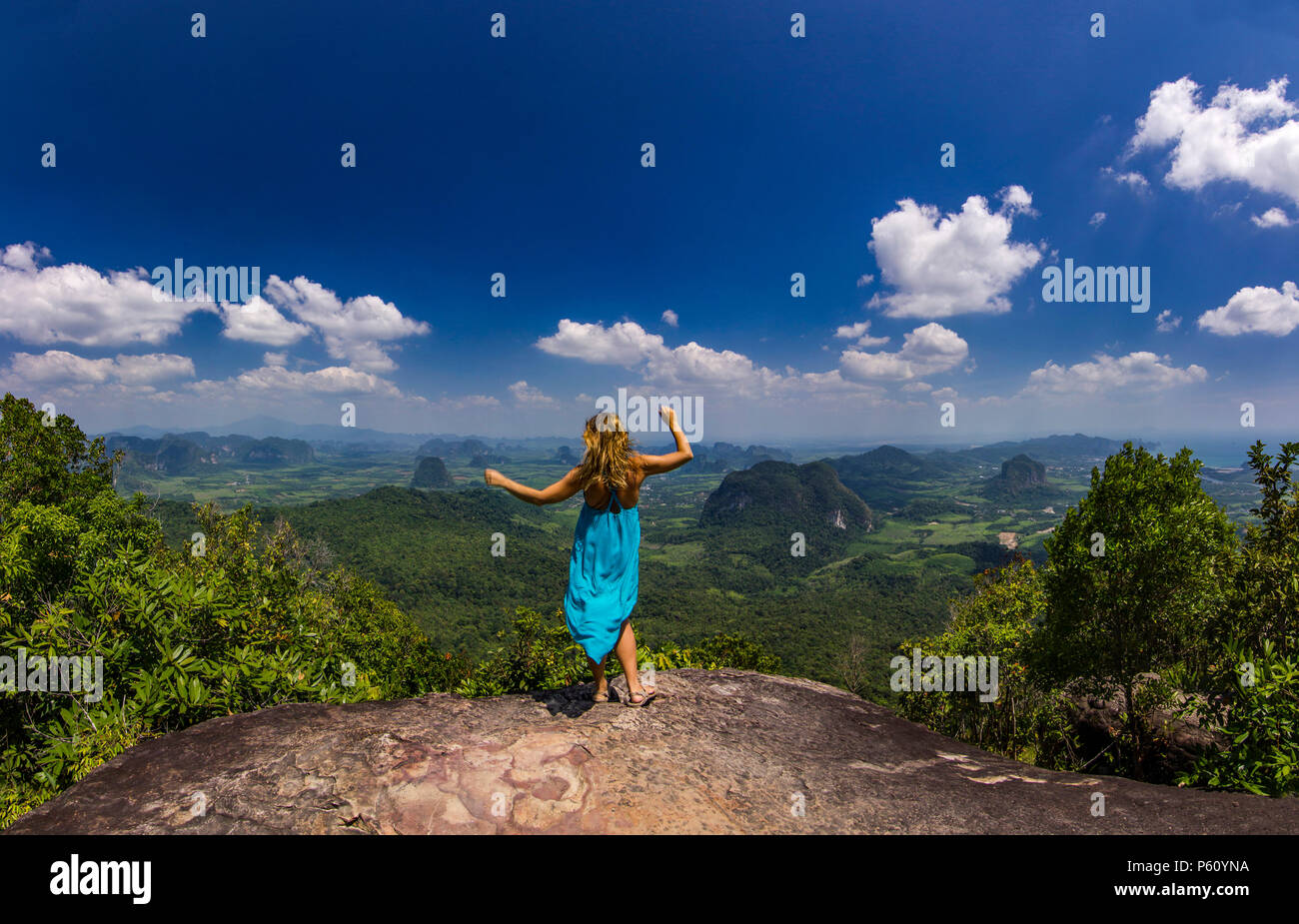 La ragazza con le mani fino in piedi sulla roccia al tramonto con le montagne al di sotto di Foto Stock