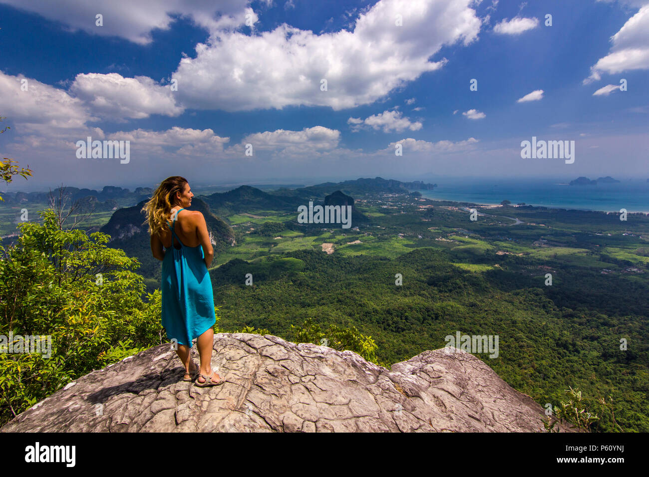 La ragazza con le mani fino in piedi sulla roccia al tramonto con le montagne al di sotto di Foto Stock