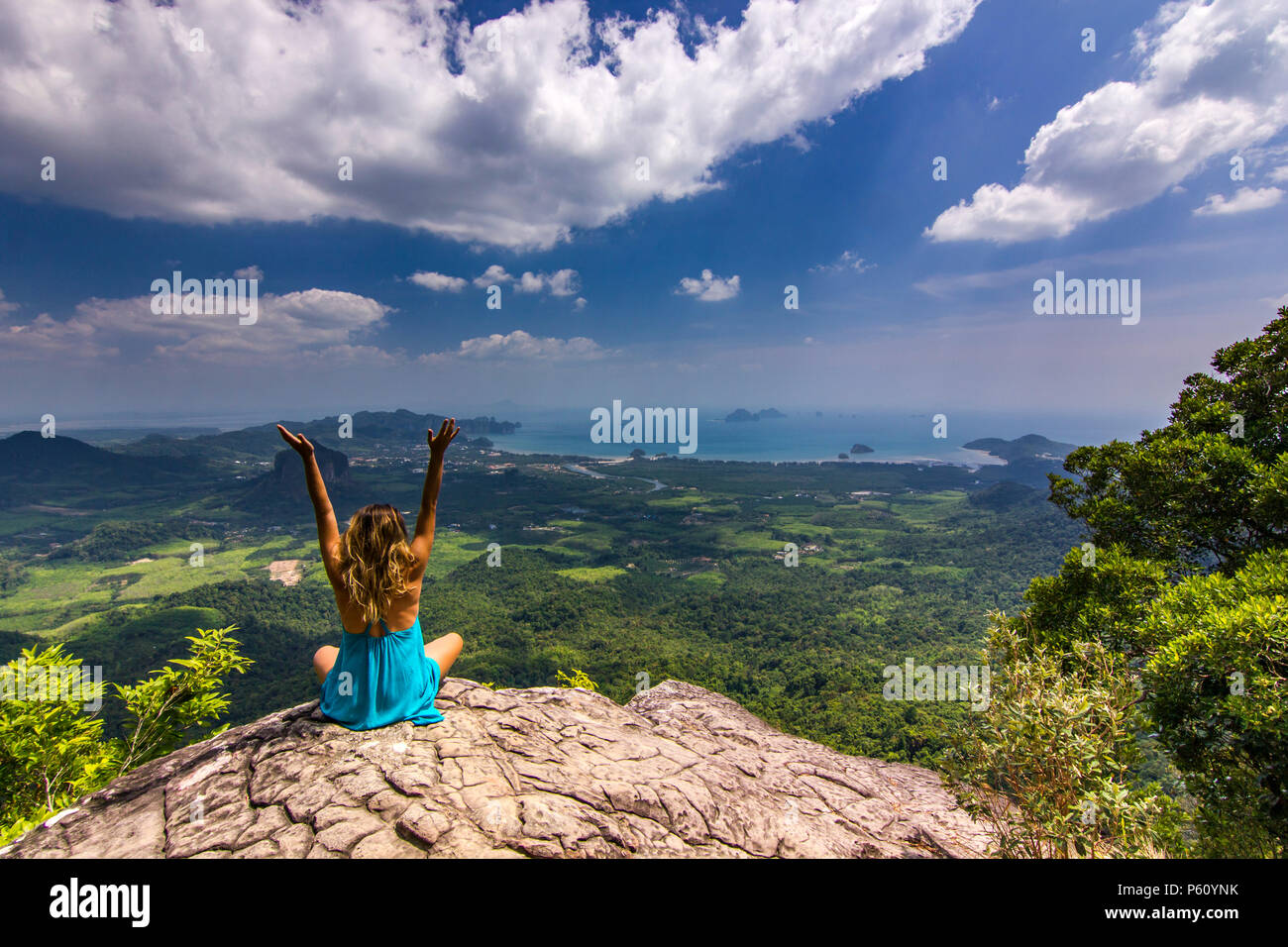 La ragazza con le mani fino seduto sulla roccia alla luce del giorno con le montagne al di sotto di Foto Stock