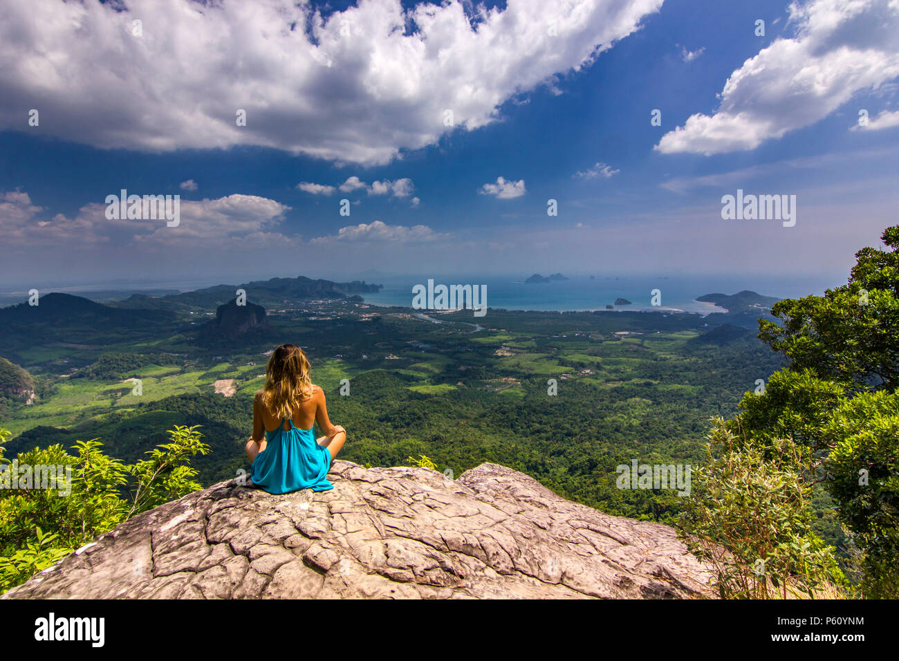 Ragazza seduta sulla roccia alla luce del giorno con le montagne al di sotto di Foto Stock