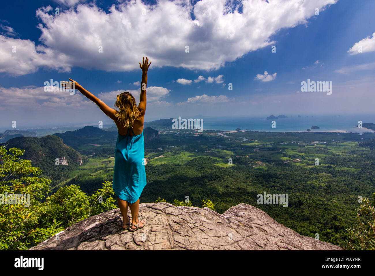 La ragazza con le mani fino in piedi sulla roccia al tramonto con le montagne al di sotto di Foto Stock