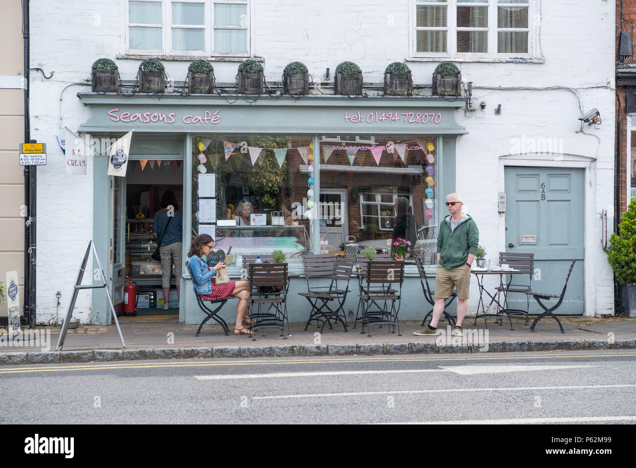 Donna seduta al tavolo della pavimentazione e uomo in piedi al di fuori delle stagioni Deli Cafe in Piazza del Mercato, Amersham Città Vecchia,Buckinghamshire, Inghilterra, Regno Unito Foto Stock