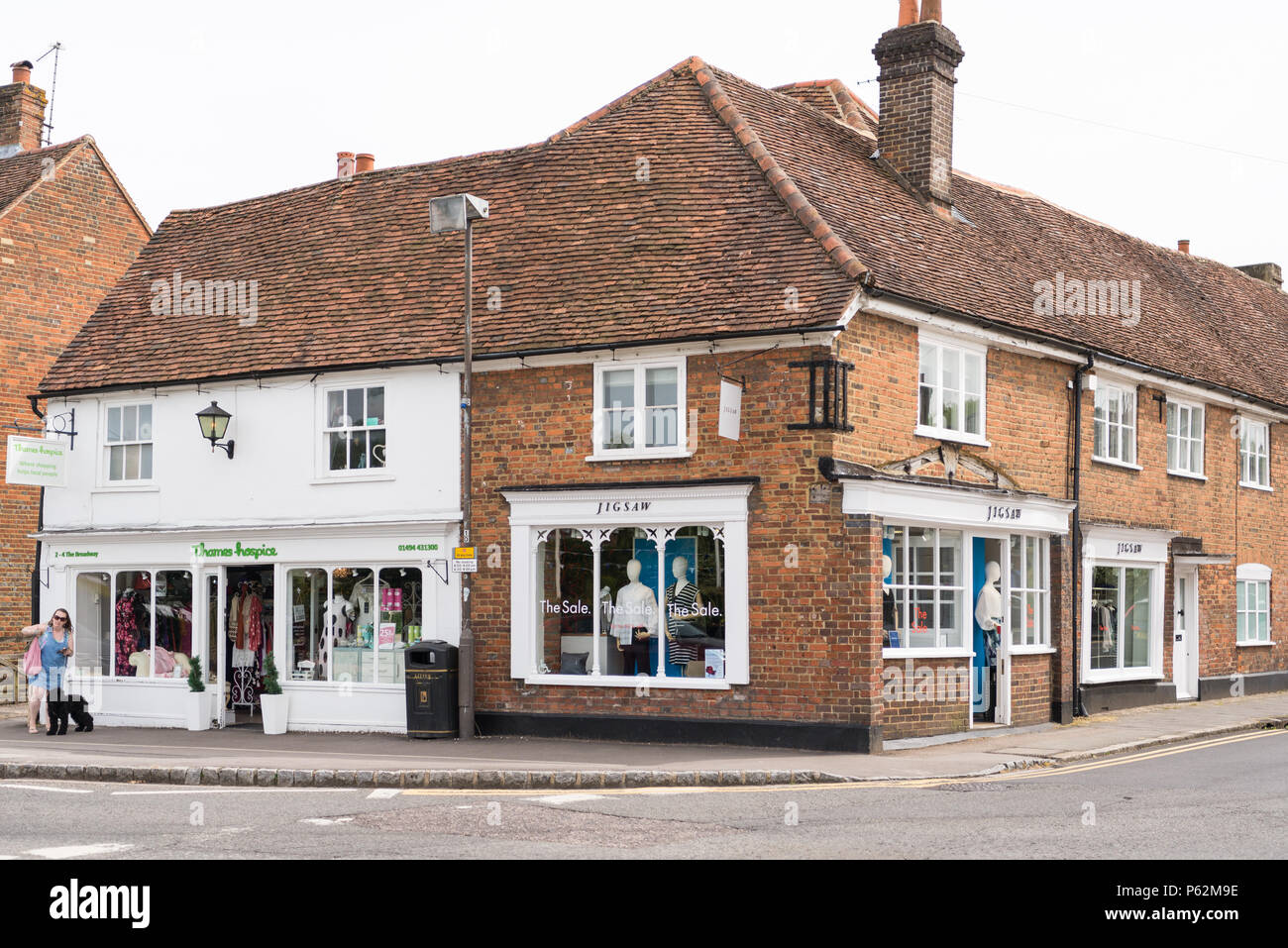 Donna con un cane nero al guinzaglio passa il Tamigi Ospizio shop e boutique di Jigsaw, Amersham Città Vecchia, Buckinghamshire, Inghilterra, Regno Unito Foto Stock