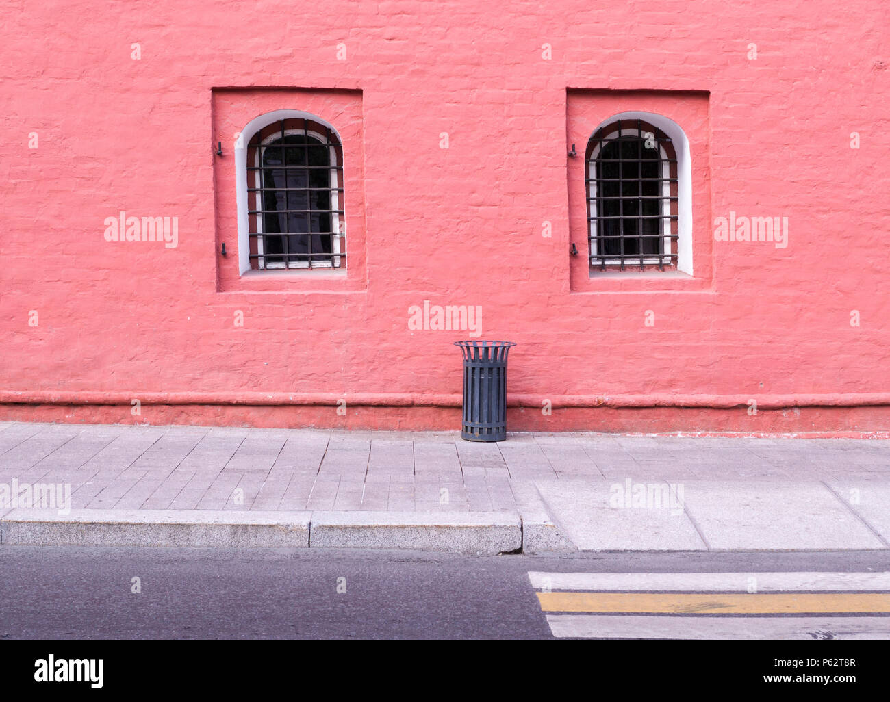 Muro di mattoni dipinto di rosso con finestra di reticolo e spazzatura vicino al marciapiede. sfondo, architettura Foto Stock