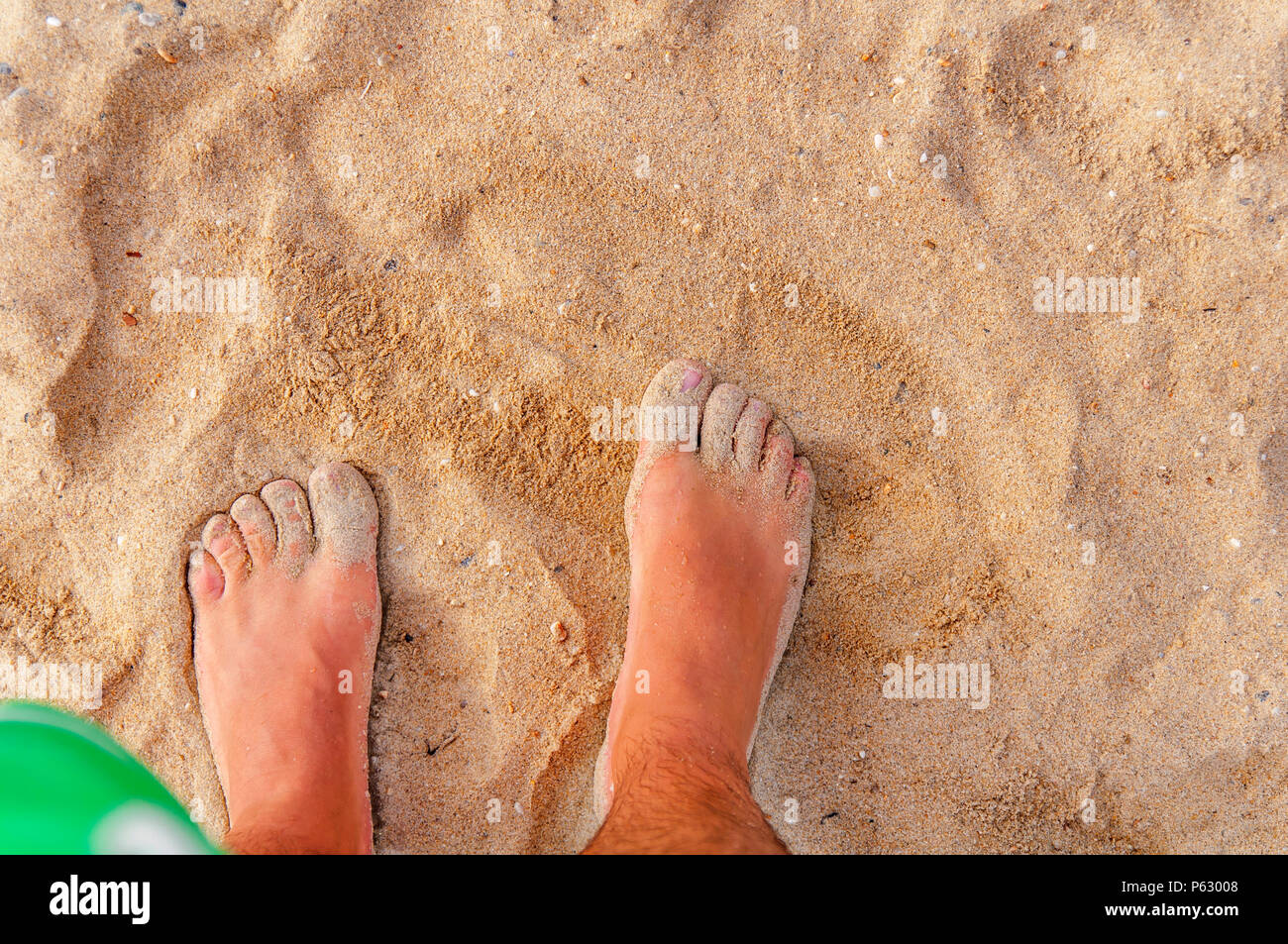 L uomo sta nel mare e guarda al suo piede nella sabbia e acqua Foto Stock