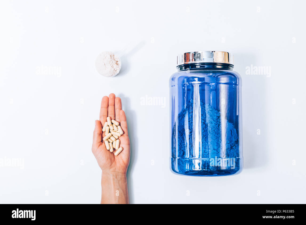 Immagine minimale di di nutrizione sportiva supplementi, vista dall'alto su un solido bianco sullo sfondo. Big Blue jar di proteine in polvere, scoop e donna di mano con pi Foto Stock