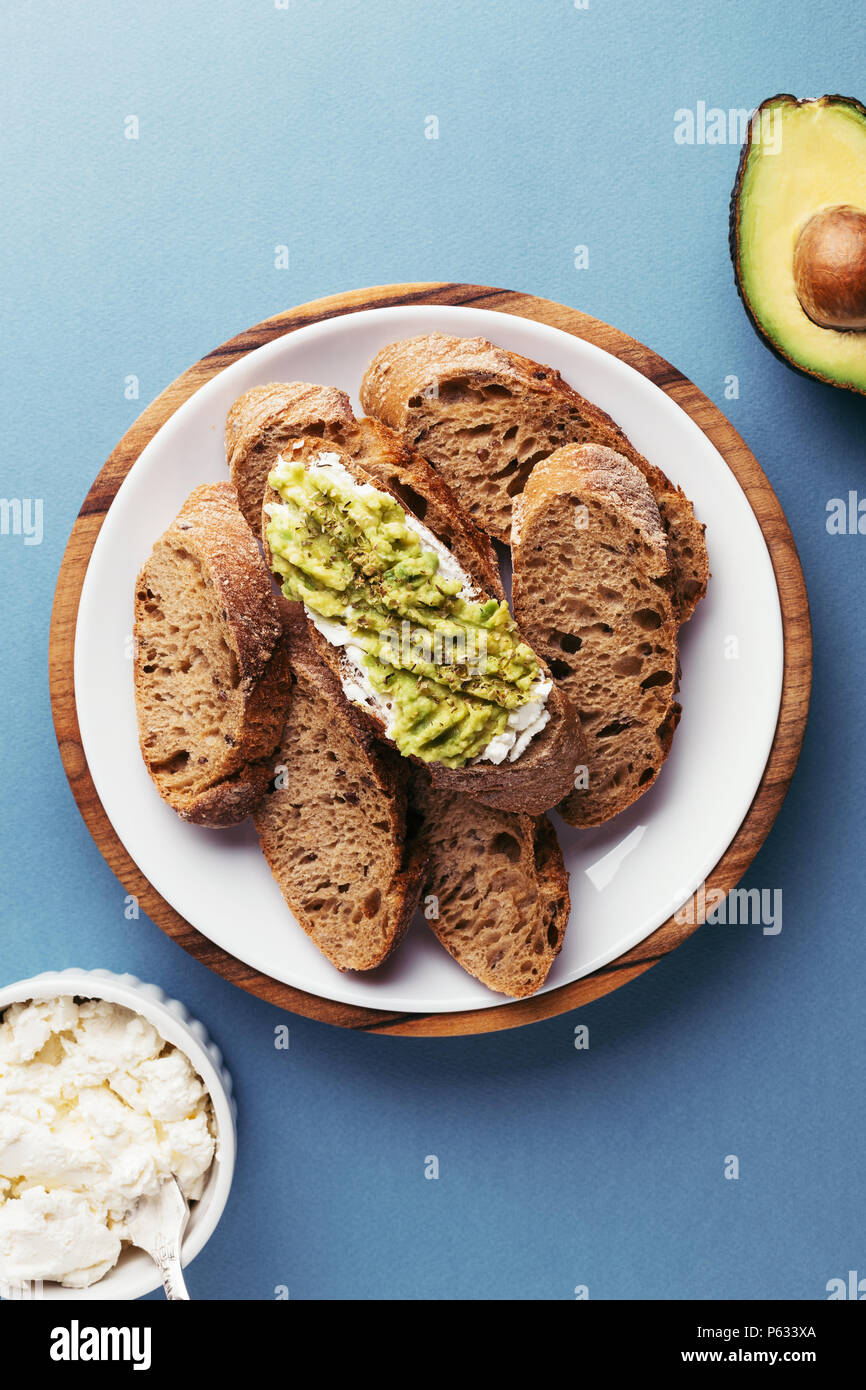 Bruschetta con crema di formaggio e avocado, francese baguette tritato sulla piastra e di avocado su sfondo blu. Vista dall'alto. Foto Stock