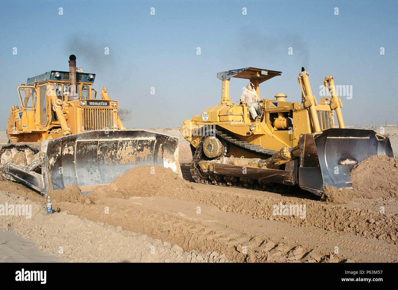 Un gatto e un bulldozer Komatsu gara lungo il livellamento del terreno nel deserto per strada la costruzione di base e successivamente di asfaltatura. Dubai, EAU. Foto Stock