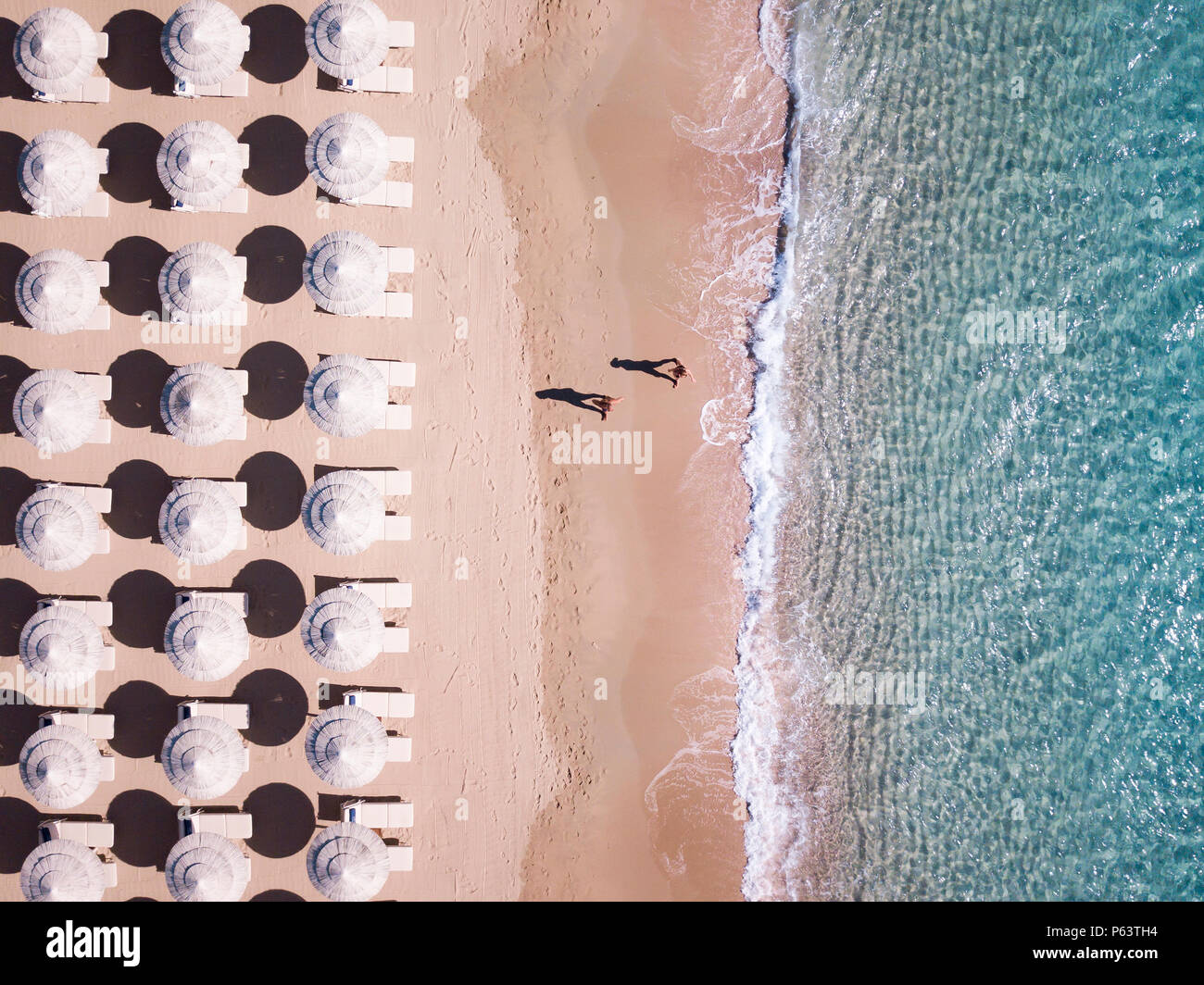 Vista aerea del fantastico mare turchese con bianchi ombrelloni e sedie a sdraio. Due persone sono a piedi sulla riva. Bella e soleggiata giornata estiva in Sardini. Foto Stock