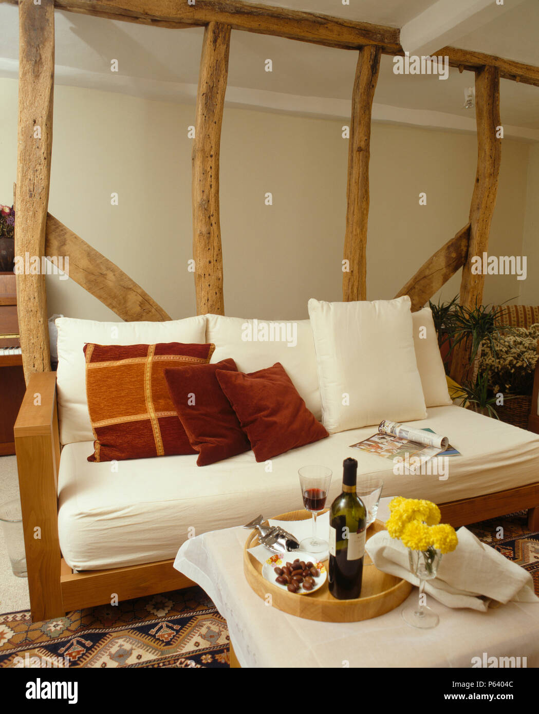 La crema divano sottostante parete di travi con intonaco rimosso in cottage soggiorno Foto Stock