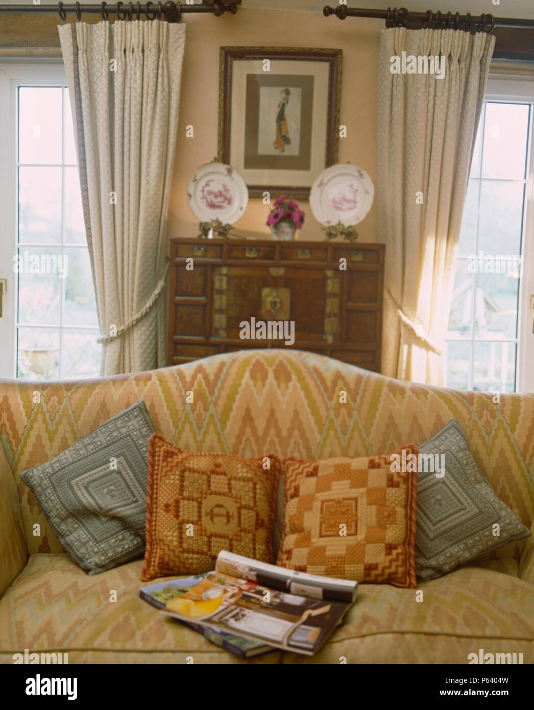 Arazzo cuscini e rivista aperta sulla stampa del Bargello divano in cottage soggiorno con drappi crema sulla finestra Foto Stock