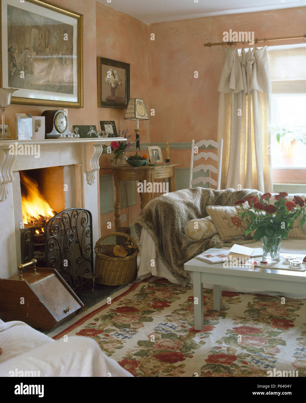 Il carbone di antiquariato grembiale e ferro battuto fireguard sul camino in cottage soggiorno con tappeto floreale e divano con pelliccia di buttare Foto Stock