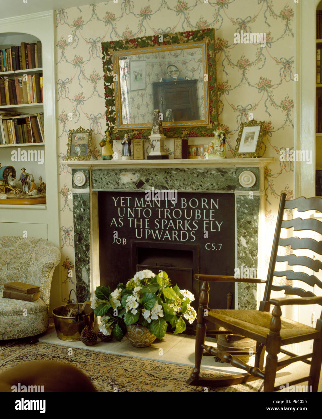 Viintage sedia a dondolo accanto al camino con iscritto testo religioso in salotto con carta da parati floreale Foto Stock