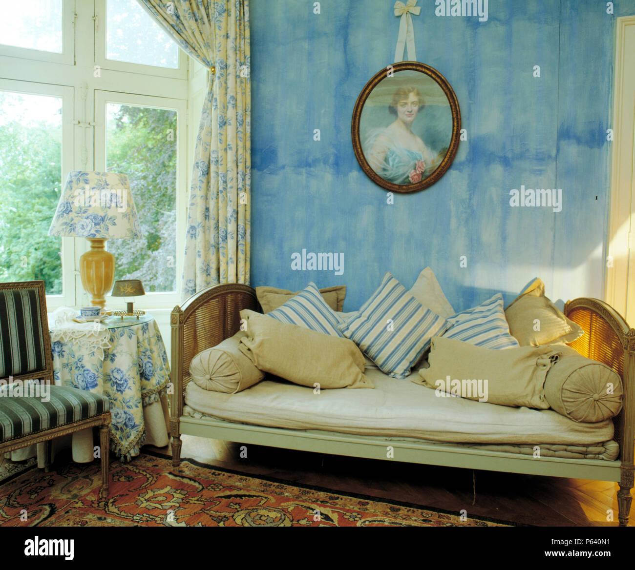 Blu Vernice di trascinamento-effetto muro con vintage ritratto sopra il Francese letto da giorno in Francese soggiorno con blu tende floreali Foto Stock