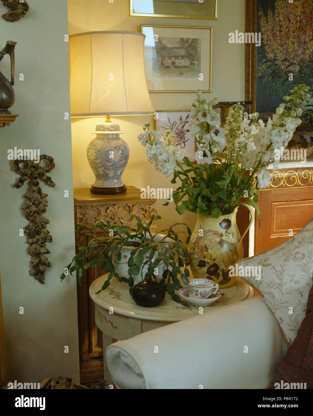 Lampada accesa e la disposizione di bianco delphiniums sul piccolo tavolo circolare in cottage soggiorno Foto Stock