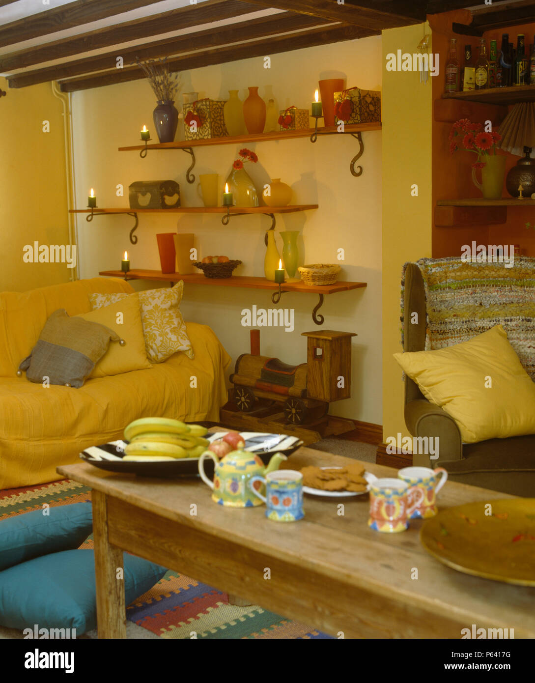 Semplice tavolo da caffè in legno in giallo cottage la stanza di seduta con candele su scaffalature di legno Foto Stock