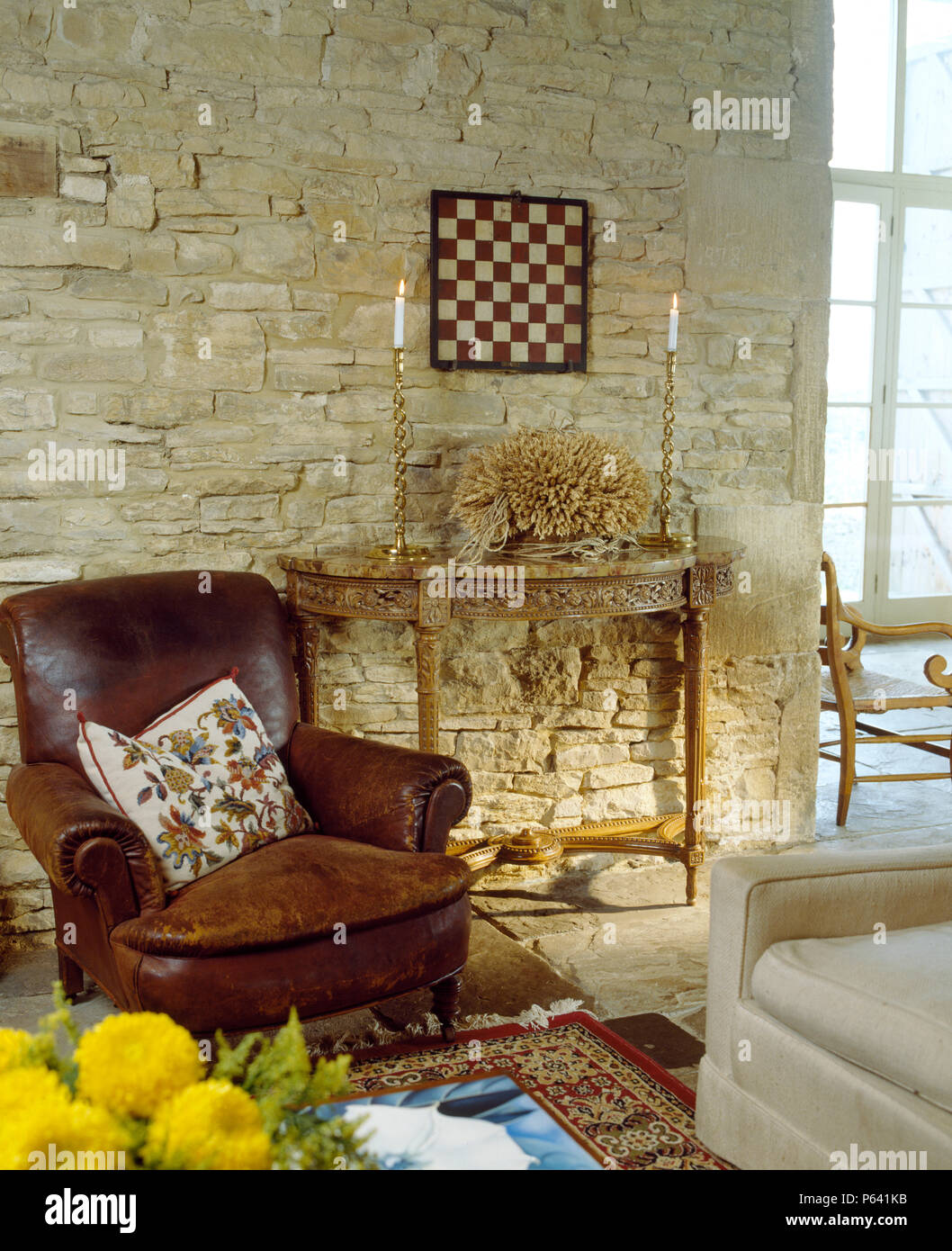 In pelle marrone poltrona accanto all antico tavolo console nel fienile conversione stanza vivente con pietra esposta parete Foto Stock