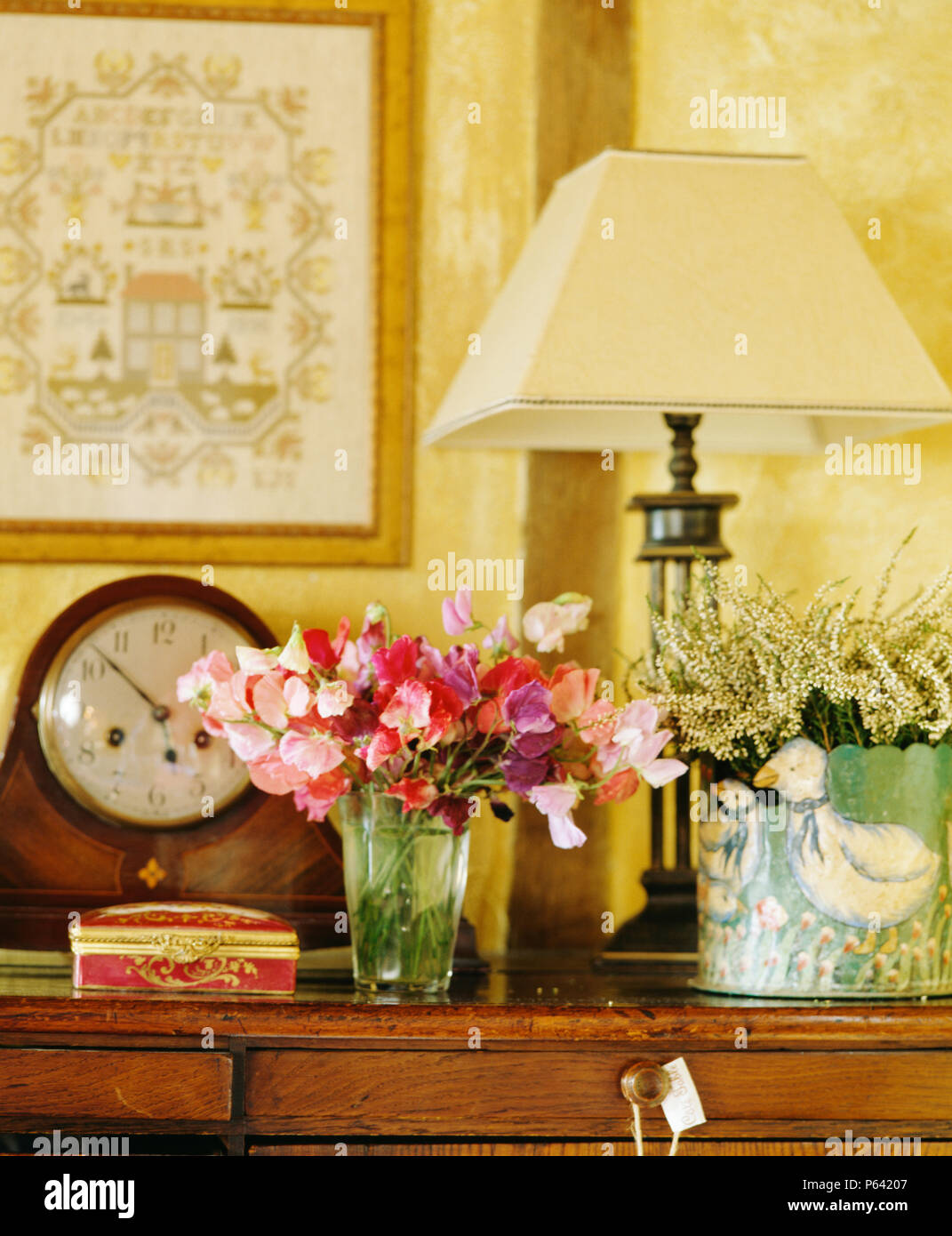 Close-up di vaso di sweetpeas con crema di lampada e antico orologio sul tavolo antico Foto Stock