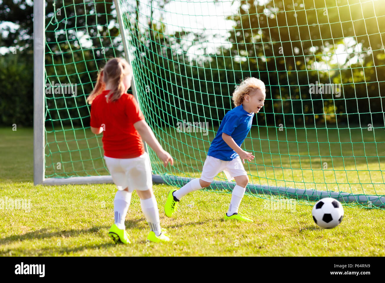 I bambini giocano a calcio sul campo all'aperto. Bambini segnare un gol a  partita di calcio. Ragazzo e una ragazza calci palla. Bambino che corre in  team jersey e placchette. La scuola