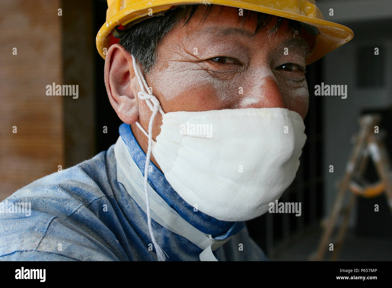 Un Lavoratore che indossa una maschera di cotone mette in pausa dal lavoro di levigatura intonaco del soffitto in una nuova torre di uffici a Pechino. Foto Stock