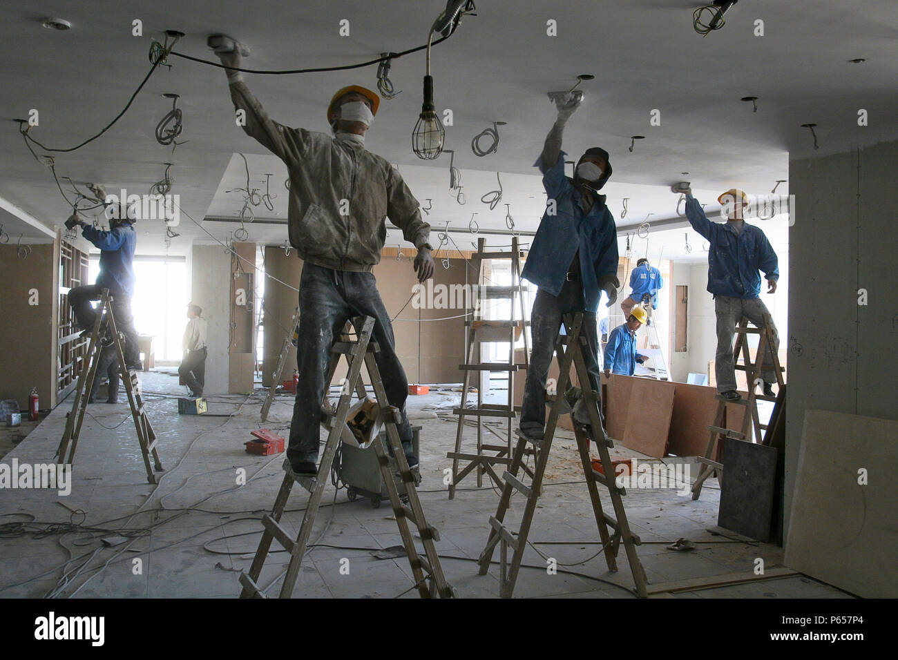 Lavoratori cinesi di levigatura intonaco del soffitto in una nuova torre di uffici a Pechino. Foto Stock