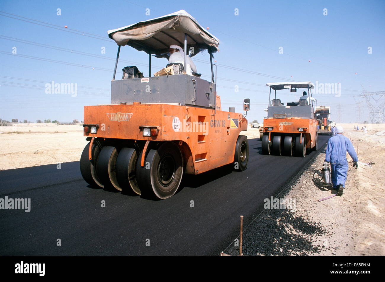 Una squadra di stanchi dei rulli viene utilizzato per il lavoro di finitura sulla superficie dell'asfalto di una strada a scivolo, Dubai, EAU. Foto Stock