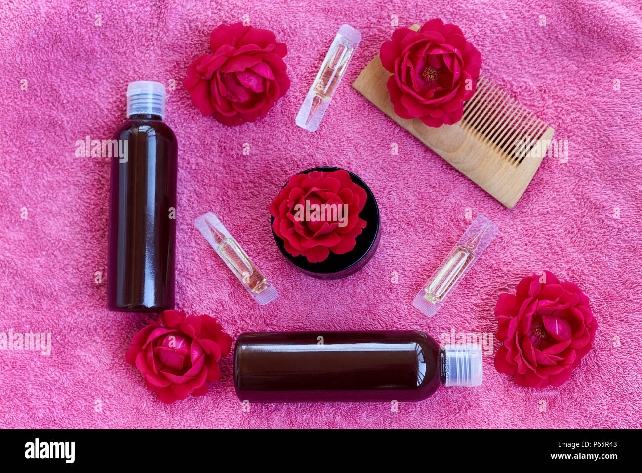 Una cura dei capelli prodotto, un pettine e boccioli di rosa rossa su un asciugamano rosa. Foto Stock