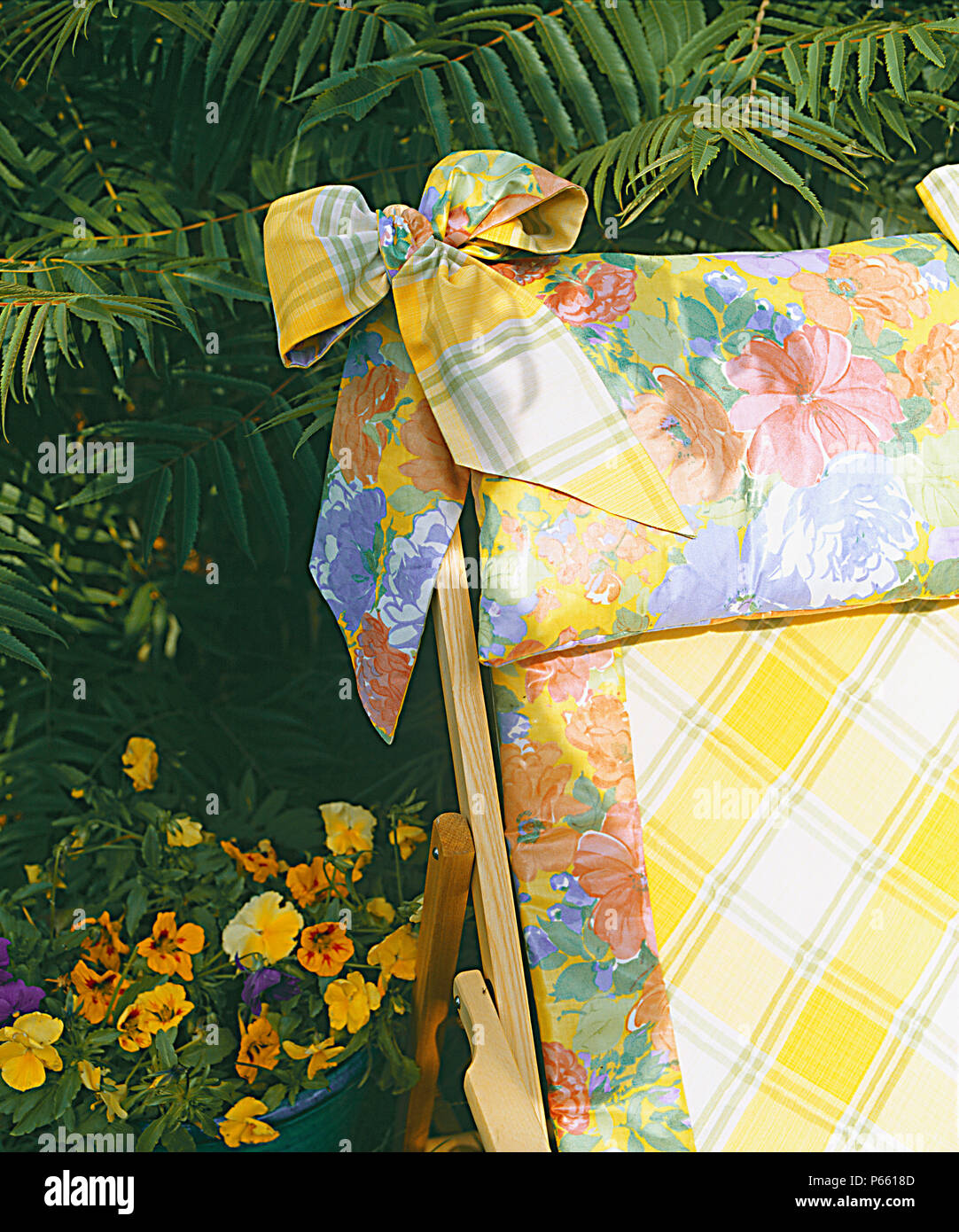 Close-up di cuscino fiorito legato con la prua sulla sedia a sdraio con giallo verifica della copertura con bordatura floreale Foto Stock