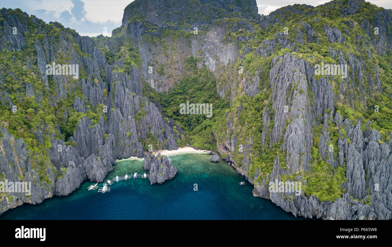 Antenna fuco vista delle barche tradizionali in una baia stretta con una bella spiaggia di sabbia e le torreggianti, frastagliate scogliere di calcare Foto Stock