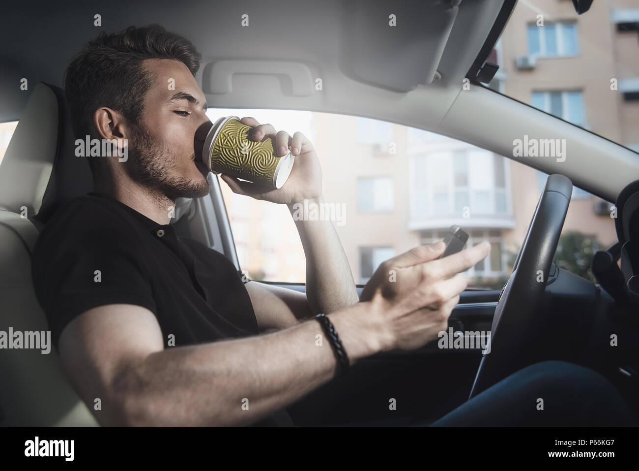 Bracci di man tenere un caffè e telefono in automobile Foto Stock