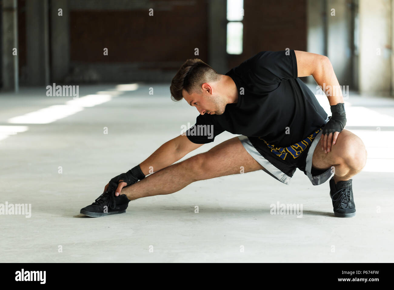 Boxer tailandese vestita di nero t-shirt e pantaloncini, pugni con bende, riscaldare il concetto, vuoto posto industriale Foto Stock