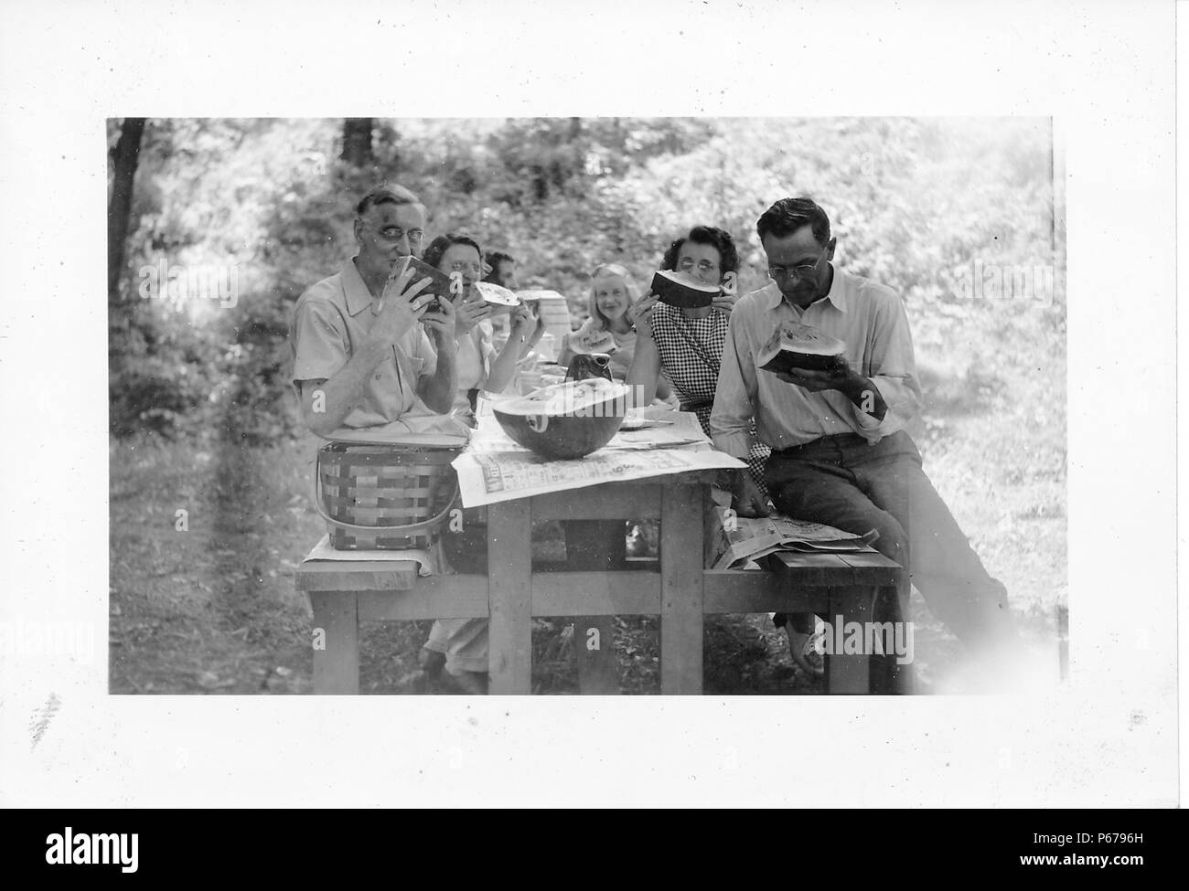 Fotografia in bianco e nero, mostrando le sei persone, compresi gli uomini, le donne e i bambini seduti attorno a un giornale-coperto tavolo da picnic, mangiare grandi pezzi di anguria, con un vintage, vimini Cesto picnic su un banco, e la metà di un cocomero sul tavolo, probabilmente fotografato in Ohio nel decennio dopo la II Guerra Mondiale, 1950. () Foto Stock