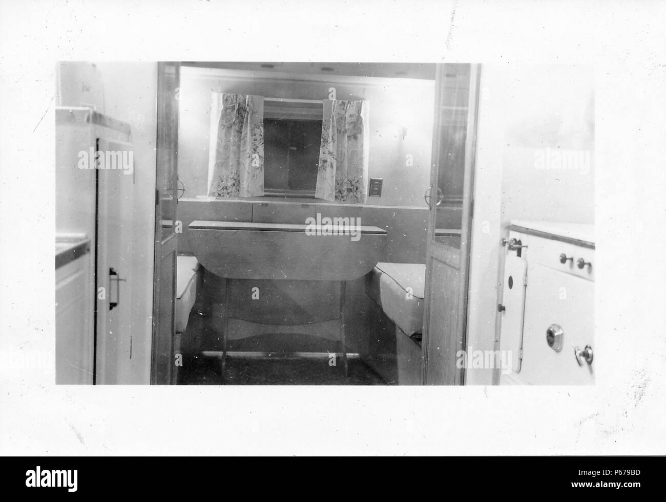 Fotografia in bianco e nero, che mostra la parte interna di un piccolo, metà del secolo il caravan o rimorchio home, con fornelli e frigorifero di destra e di sinistra in primo piano, e letti, una struttura di tavolo pieghevole e una piccola finestra con tende dai motivi floreali visibile attraverso aprire le porte doppie, probabilmente fotografato in Ohio nel decennio dopo la II Guerra Mondiale, 1950. () Foto Stock