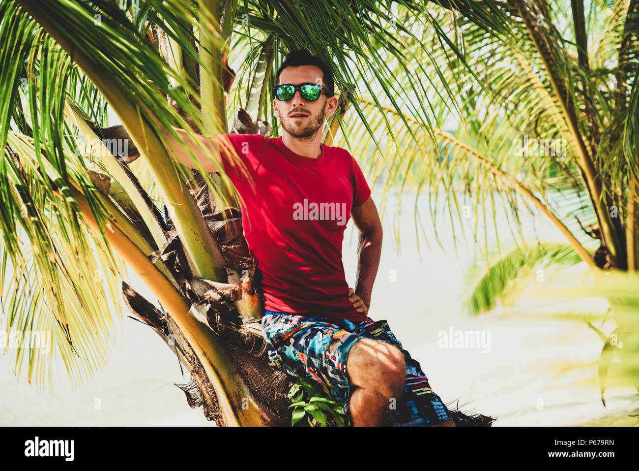 Estate Vacanze di viaggio. Uomo bello in occhiali da sole a prendere il sole in spiaggia tropicale su sfondo Palm tree e il mare Foto Stock