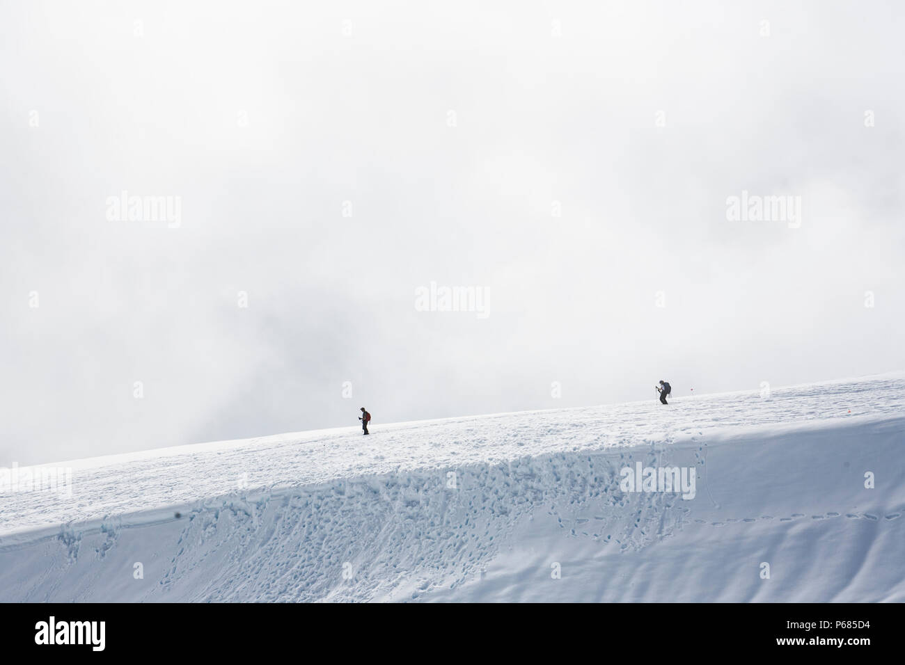 Due escursionisti / alpinisti discendente da ghiacciai e campi di neve del monte Rainier come nuvole basse di salita e di caduta intorno a loro, Mount Rainier National Foto Stock