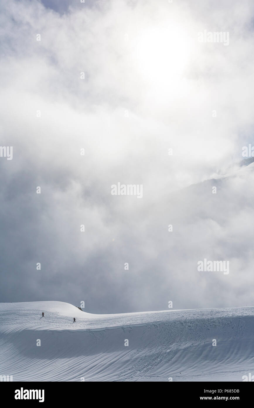 Due piccole figure umane scendendo una coperta di neve cresta come il sole fa capolino tra le nuvole in aumento, il Parco Nazionale del Monte Rainier, Washington, Stati Uniti d'America. Foto Stock