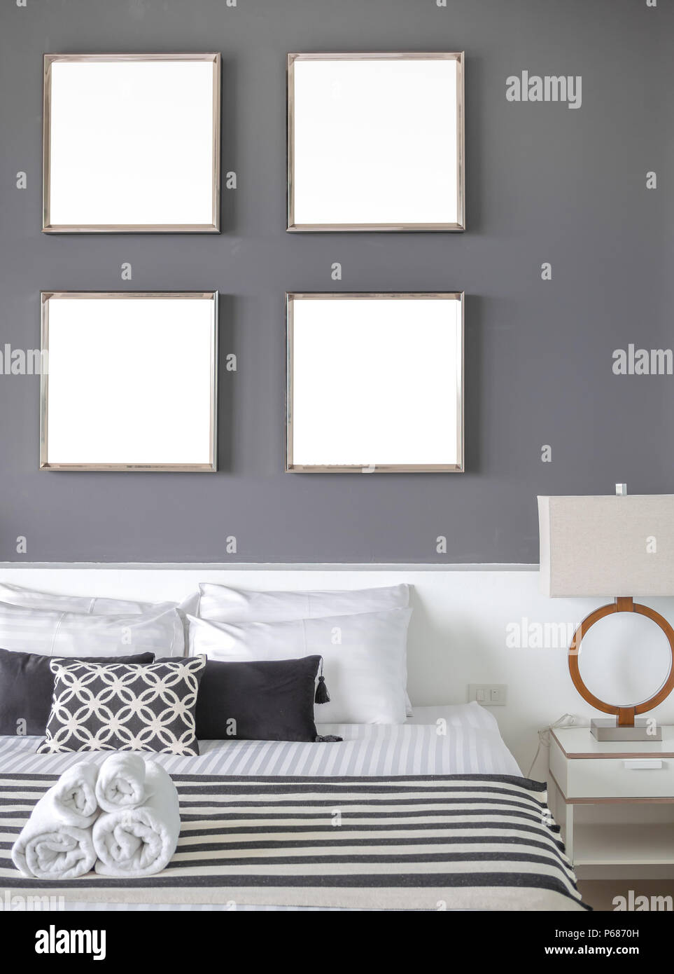 Camera moderna con quattro quadrati di Blank intelaiature in acciaio inossidabile sul muro grigio interno, cuscini e asciugamani sul letto con luce laterale. Foto Stock