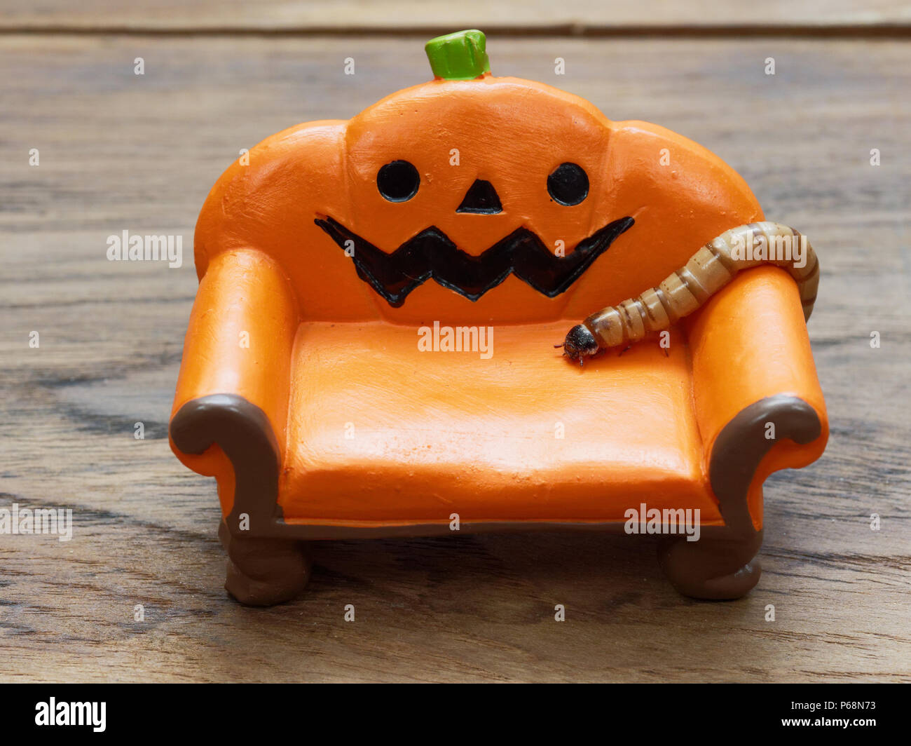 Super o worm gigante strisciando sulla miniatura arancione zucca ceramica lettino o divano scuro su una superficie di legno con una copia dello spazio utilizzato come sfondo di Halloween, ornamento, celebrazione e decorazione Foto Stock