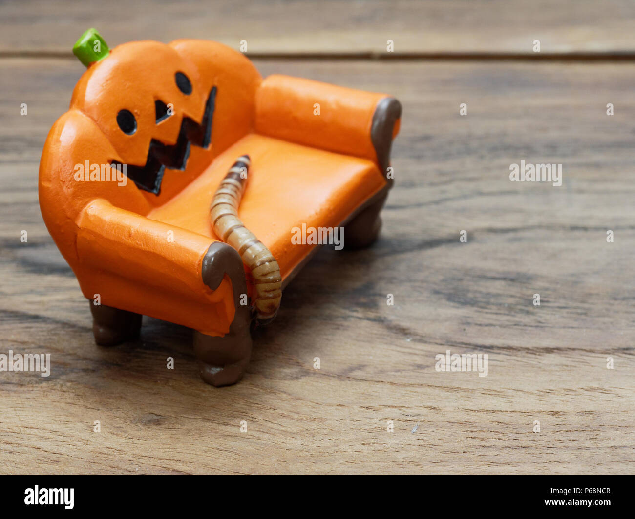 Super o worm gigante strisciando sulla miniatura arancione zucca ceramica lettino o divano scuro su una superficie di legno con una copia dello spazio utilizzato come sfondo di Halloween, ornamento, celebrazione e decorazione Foto Stock