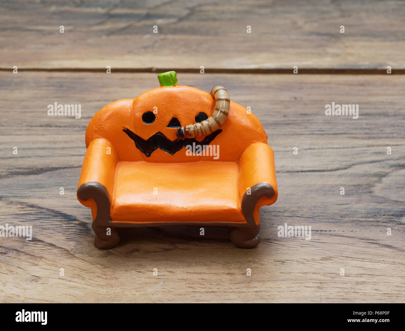 Super o worm gigante strisciando sulla miniatura arancione zucca ceramica lettino o divano scuro su una superficie di legno con una copia dello spazio utilizzato come sfondo di Halloween, ornamento, celebrazione e decorazione Foto Stock