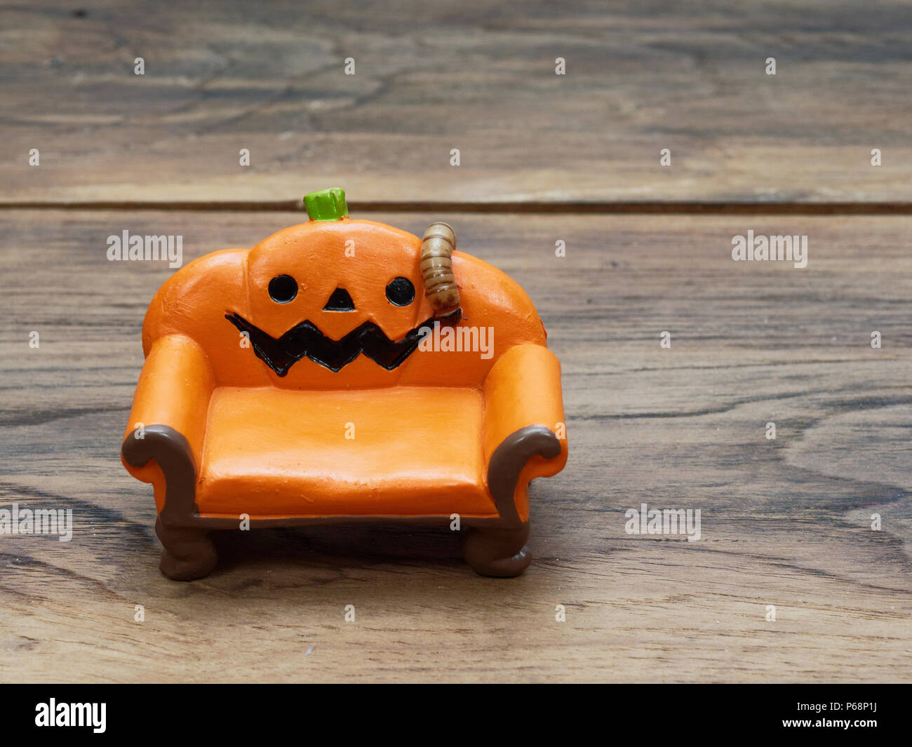 Super o worm gigante strisciando sulla miniatura arancione zucca ceramica lettino o divano scuro su una superficie di legno con una copia dello spazio utilizzato come sfondo di Halloween, ornamento, celebrazione e decorazione Foto Stock