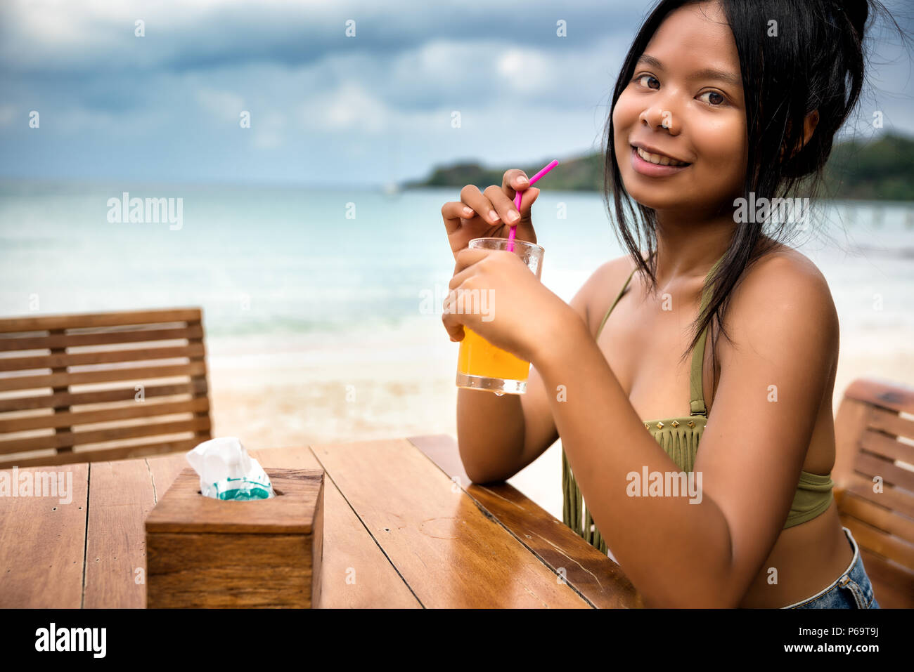 Giovane ragazza turistica avente la colazione del succo di frutta fresco seduti in un caffè sul litorale della spiaggia tropicale dell'isola di Bali su sfondo paesaggio natura Foto Stock